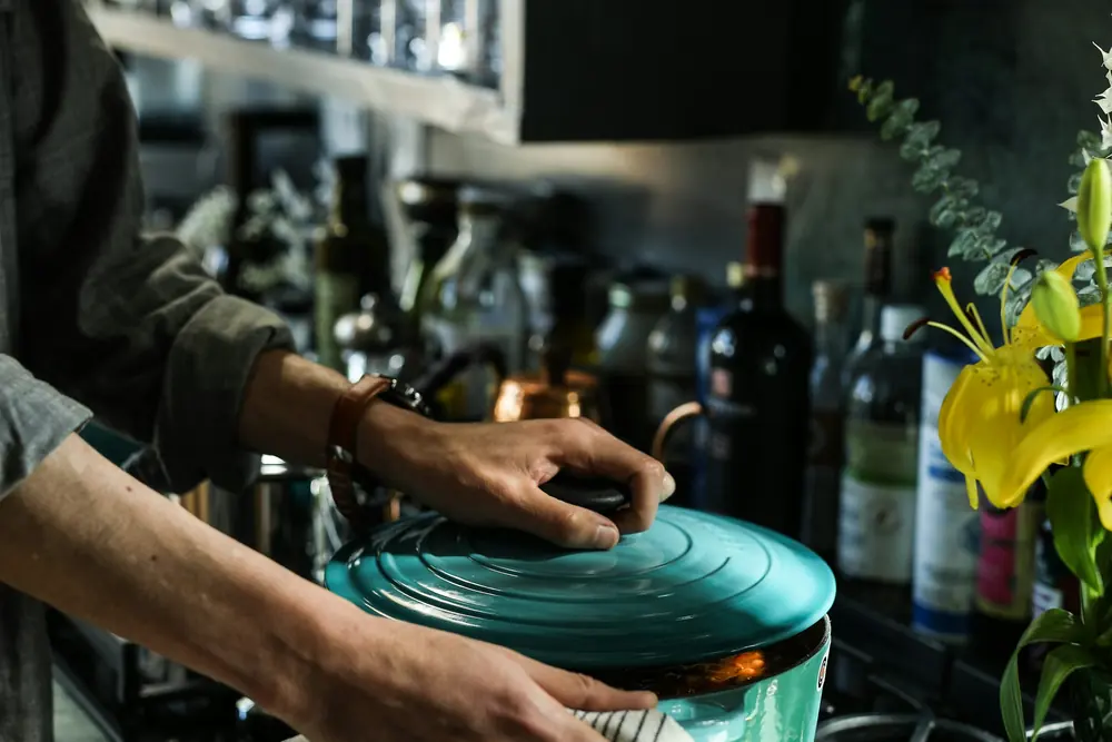 A green cooking pot being handled in a working kitchen.