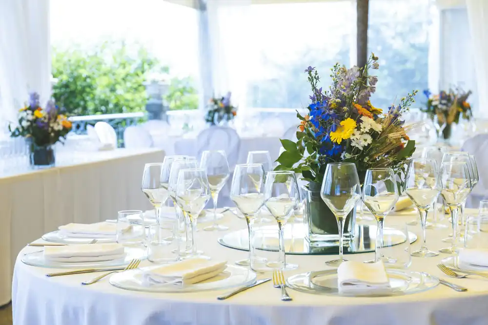 Wedding tables set with white linen, wine glasses and blue and yellow flowers.